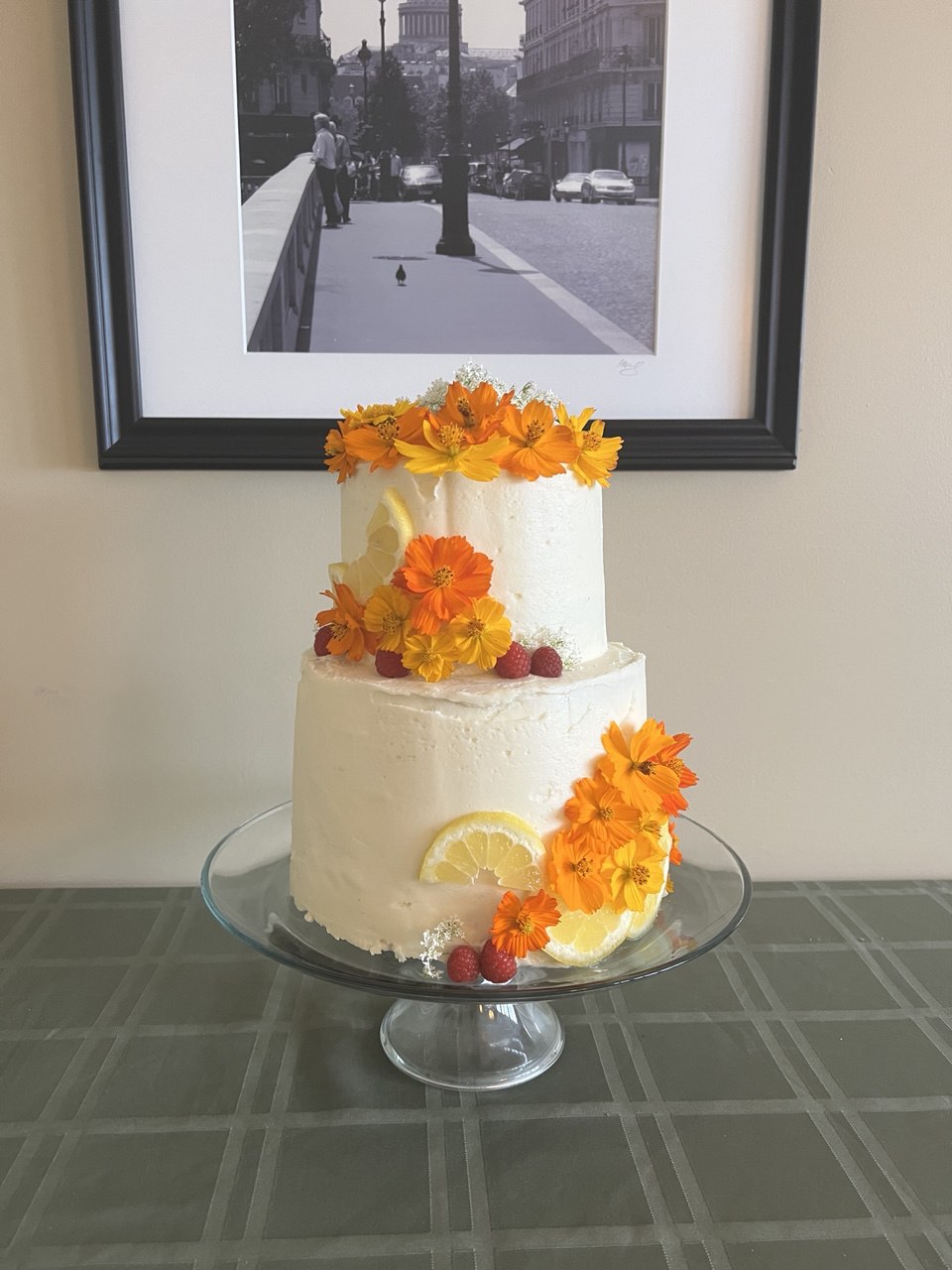 Two-tier lemon cake with edible cosmos flowers, raspberries, and lemon slices